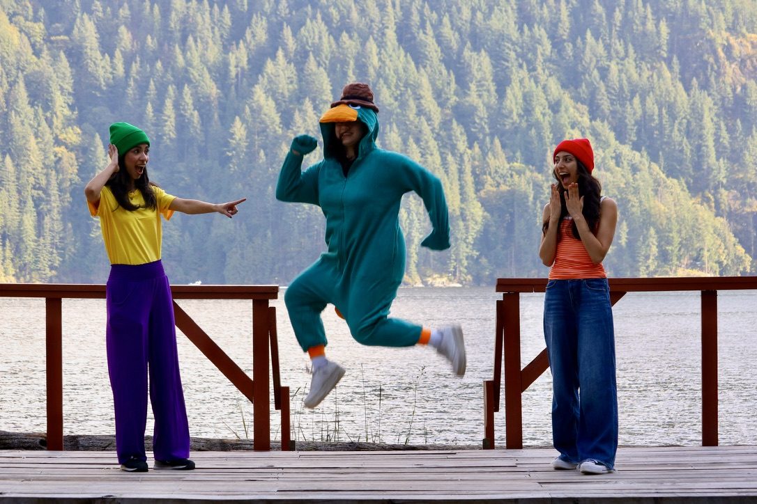 Three people dressed as Phineas, Ferb and Perry the Platypus on a lakeside dock