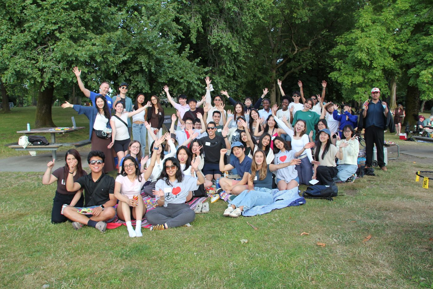 A large group of students with their hands in the air at a park social